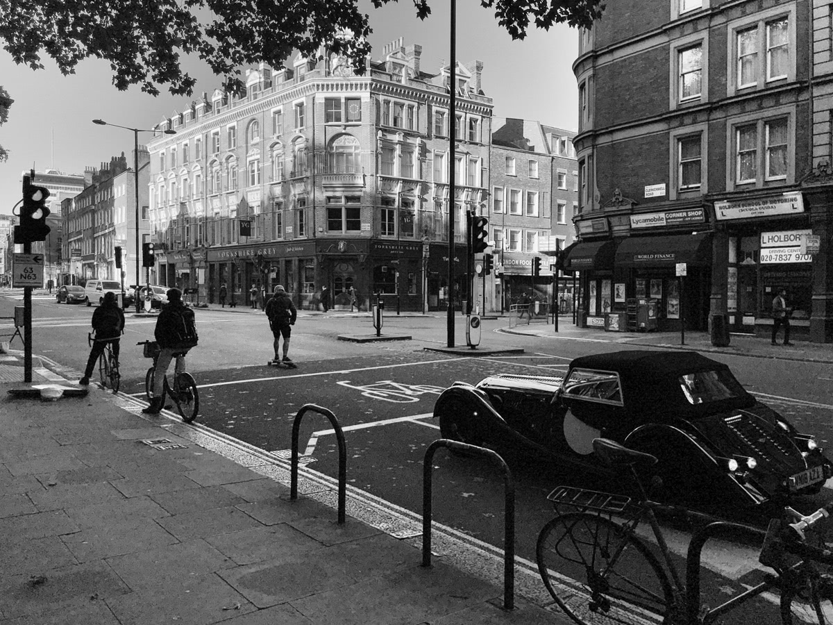 Cyclists and a vintage car wait at a crossing